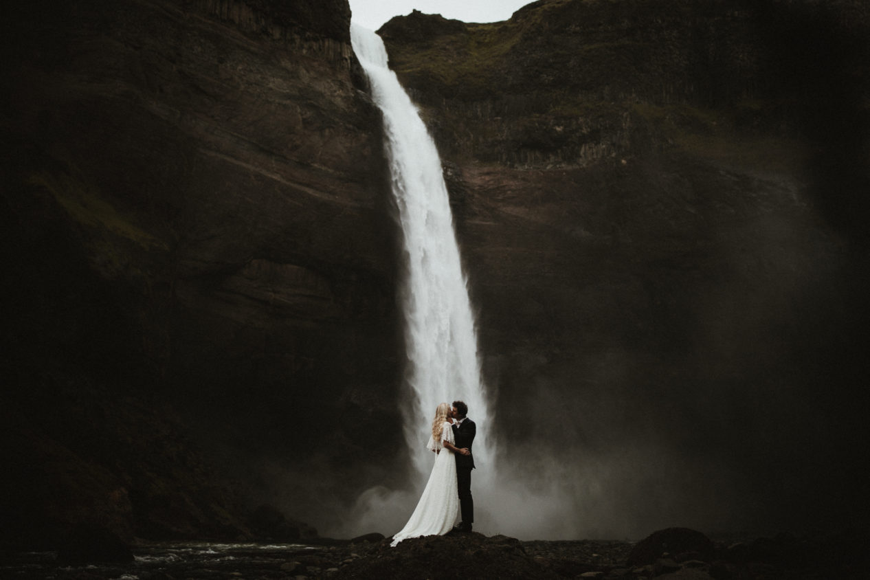 Editorial-style portrait of a couple on their wedding day under waterfall